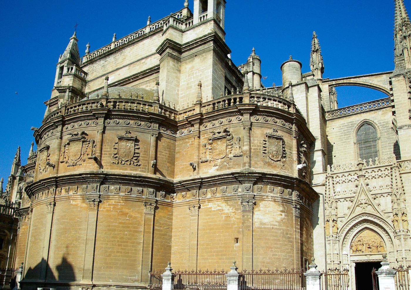 Catedral de Sevilla. La verticalidad de la arquitectura gótica se logra a través de una serie de elementos (el arco apuntado, los contrafuertes y arbotantes, los pináculos, etc.) que dirigen las fuerzas peso de la estructura hacia el suelo y evitan que los muros se abran, retirándoles la función de ser muro de carga. Al estar el peso de la estructura soportado por este entramado de elementos en lugar de por los propios muros, como sí sucede en la arquitectura románica, se pueden abrir grandes ventanas alargadas y colocar extensas y profusas vidrieras que en el arte románico eran impensables porque se comprometía la estabilidad de la estructura